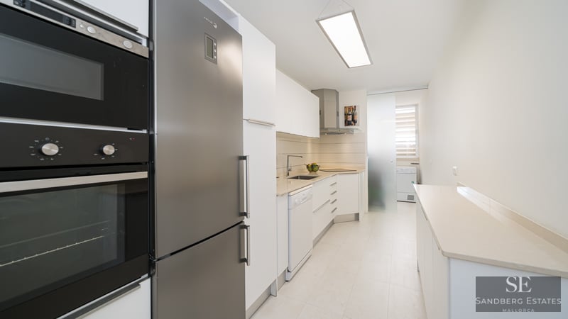 A modern galley-style kitchen with white cabinetry and stainless steel appliances.