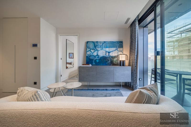 Salón moderno con sofá de bouclé blanco, arte abstracto azul y ventanales con vistas a una terraza.