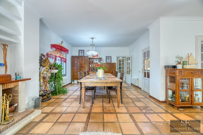 Amplio comedor con mesa de madera, suelo de baldosas de terracota, chimenea y estatua decorativa.