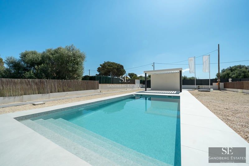Exterior view of a modern villa featuring an infinity pool, lush garden, and spacious terraces. Minimalist architecture with large windows.