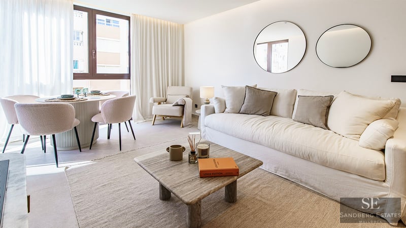 Helles Wohnzimmer mit weißem Sofa, Steintisch, runden Spiegeln und Essplatz am Fenster.