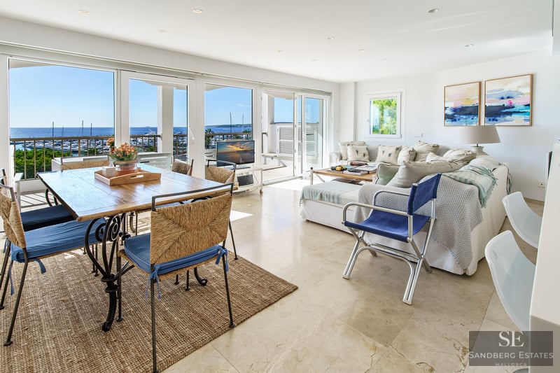 Open-plan living room with marble floors and large windows overlooking a marina and sea.