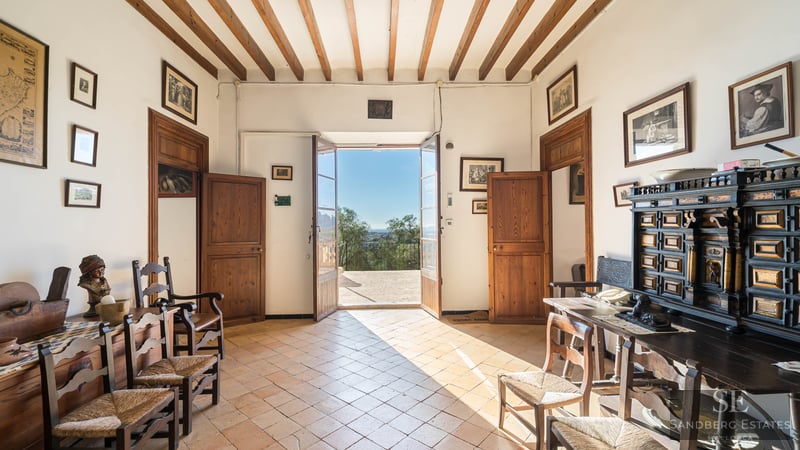 Traditional hallway with wooden beams, terracotta floors, and open doors leading to a sunny terrace.
