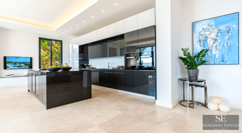Spacious modern kitchen featuring a large black glossy island, dark cabinetry, and light stone flooring.
