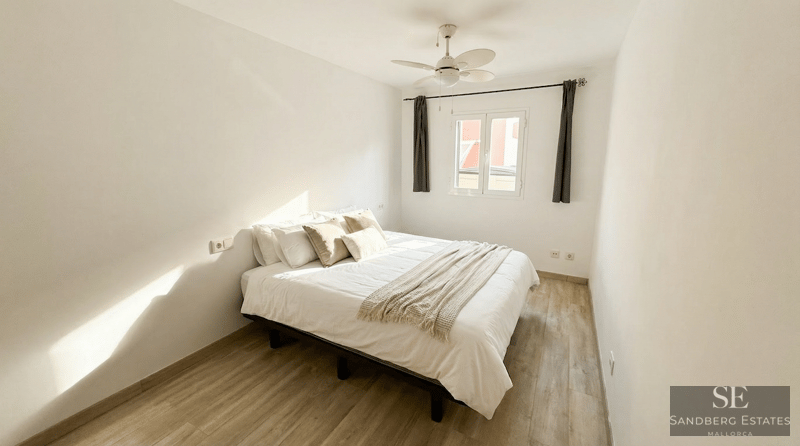 Bright bedroom featuring a white bed, light wood flooring, a white ceiling fan, and natural light.