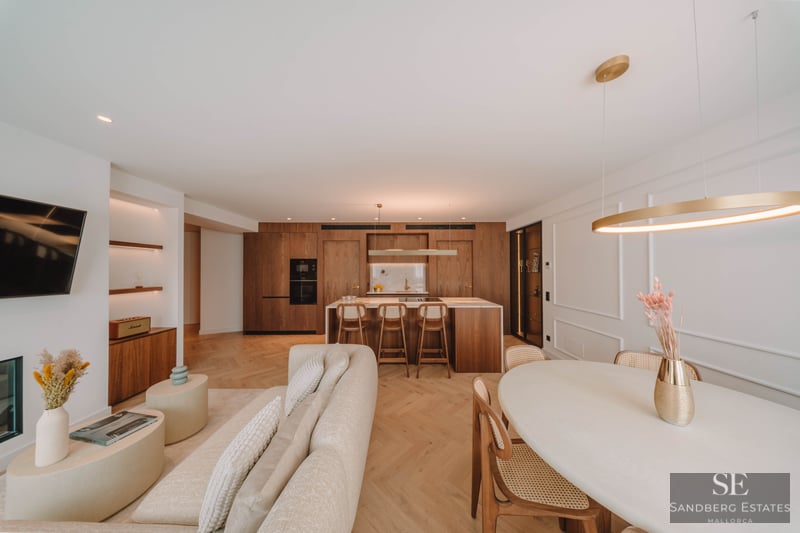 Spacious luxury living room featuring a beige sofa, herringbone wood floors, and an integrated natural wood kitchen.