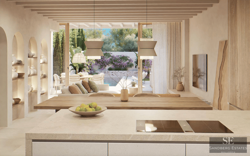 Open-plan space with a kitchen island, wooden beams, and views of a terrace with a pool and garden.