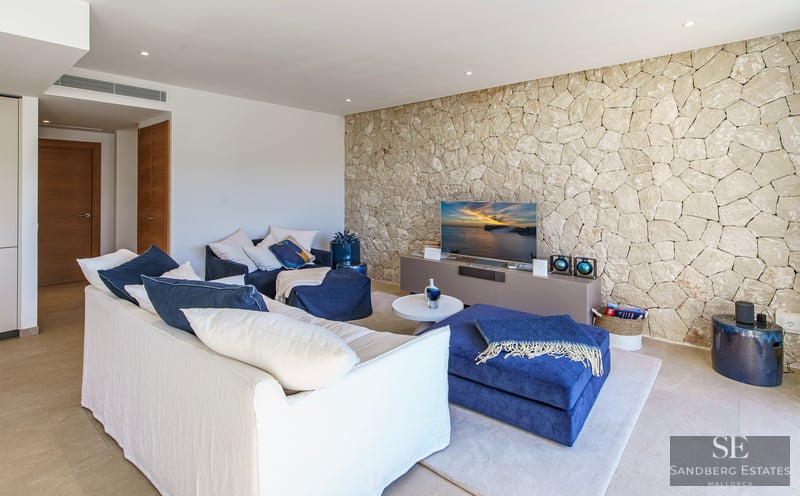 Contemporary living room featuring a white sofa, navy blue ottomans, and a textured natural stone wall with a TV.