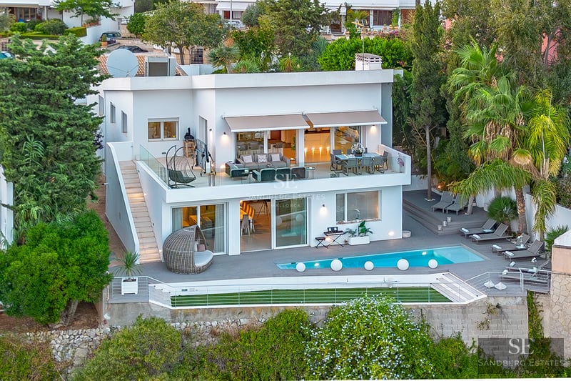 Exterior view of a modern villa featuring a pool, manicured garden, and spacious terraces. Sleek architectural design with warm lighting.