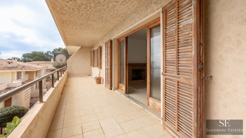 Long tiled balcony with weathered wooden shutters and glass doors leading to an indoor living area.