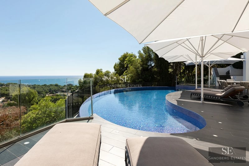 Curved infinity pool on a modern terrace with white umbrellas and loungers overlooking the Mediterranean sea.