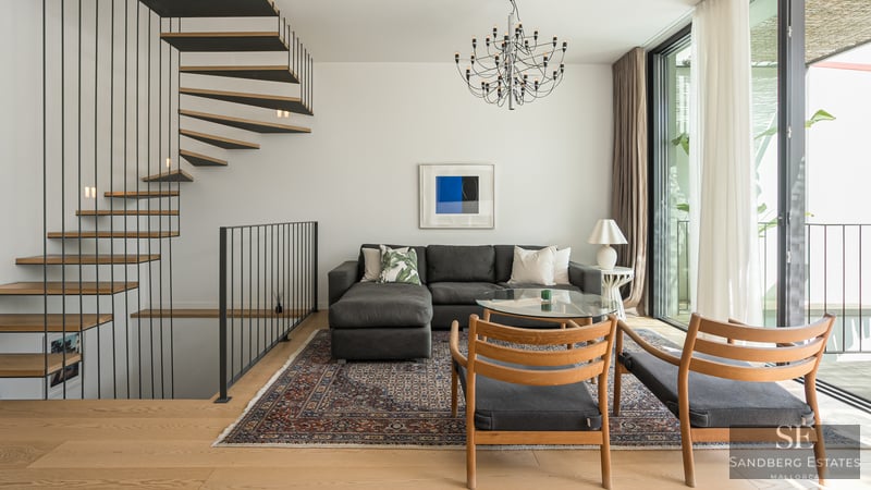 Salón contemporáneo con sofá gris, escalera de caracol de madera y grandes ventanales.