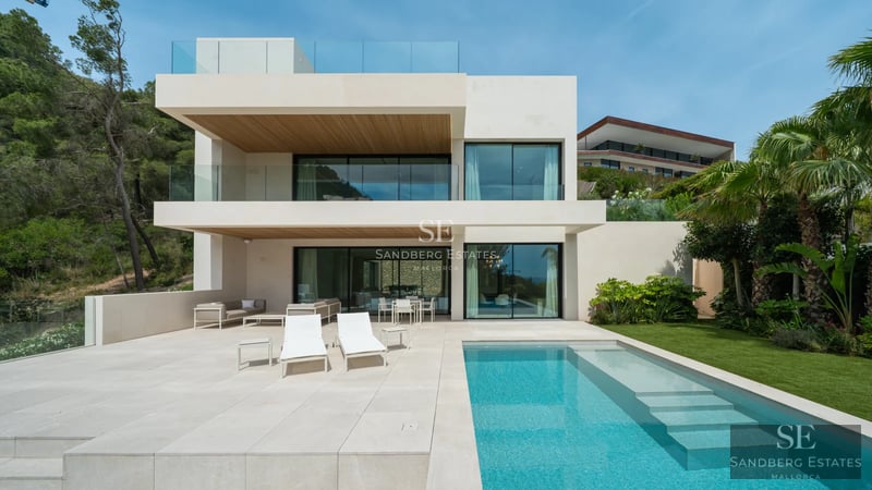 Spacious living room featuring a modern fireplace, panoramic windows, light wood floors and designer furniture in neutral tones.
