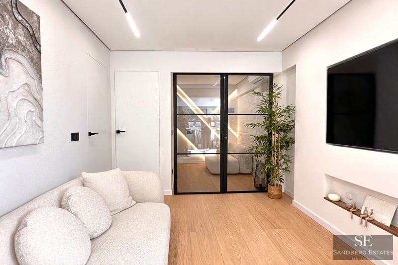 Modern living room featuring a white textured sofa, light wood floors, and black-framed glass double doors.