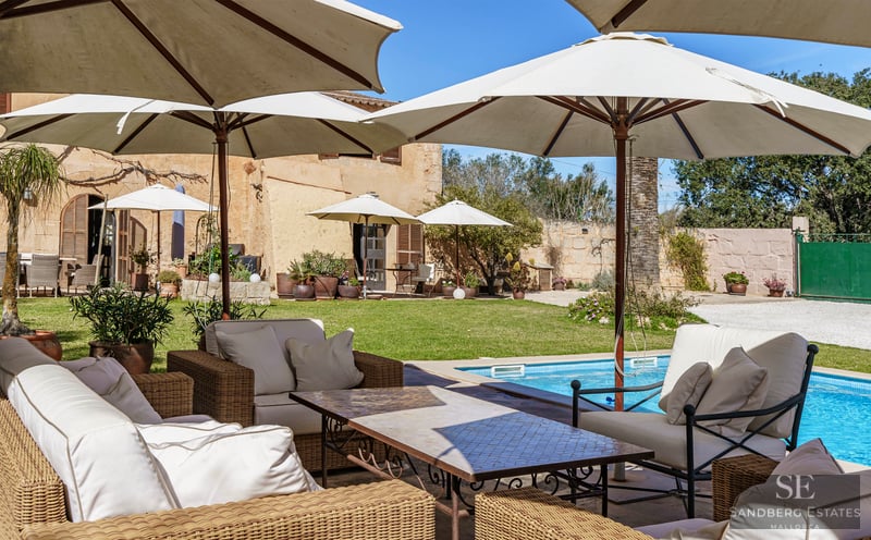 A luxury swimming pool surrounded by large white umbrellas and wicker lounge furniture in a Mediterranean garden.