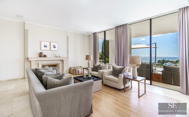 Modern living room with grey sofas, a stone fireplace, and floor-to-ceiling windows opening to a sea-view terrace.