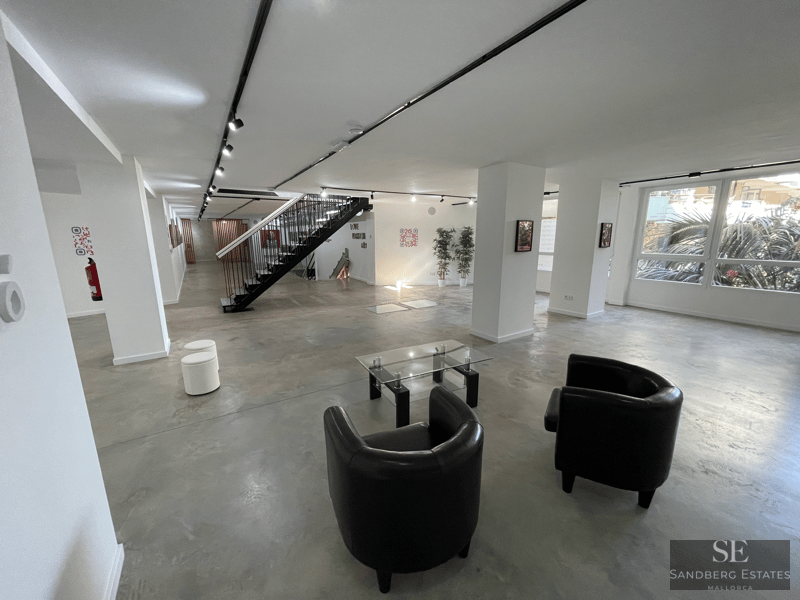 Amplio espacio con suelos de hormigón pulido, sillones de cuero negro y una escalera metálica minimalista.