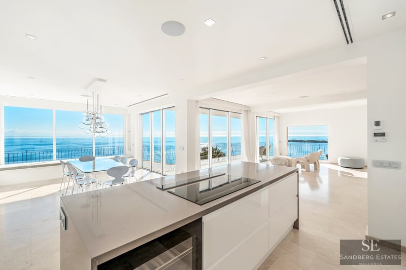 Ljust modernt kök och matsal med stora fönster som visar ett brett blått hav och klar himmel.