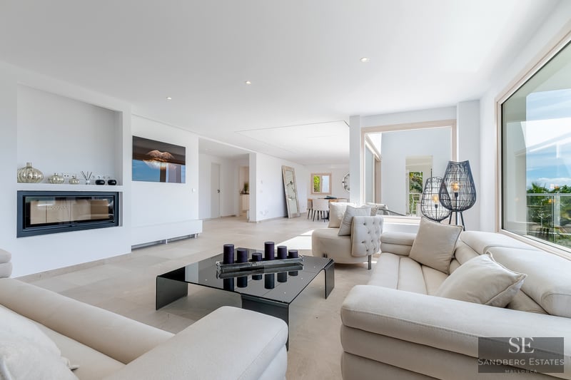 Bright living room with cream sofas, black glass coffee table, built-in fireplace, and large panoramic windows.
