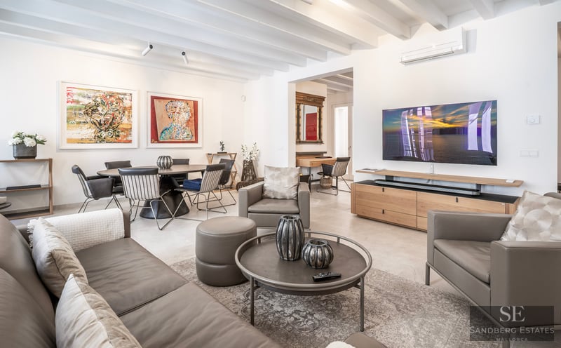 Spacious modern living room with grey leather sofas, wooden ceiling beams, large TV, and adjacent dining area with art.