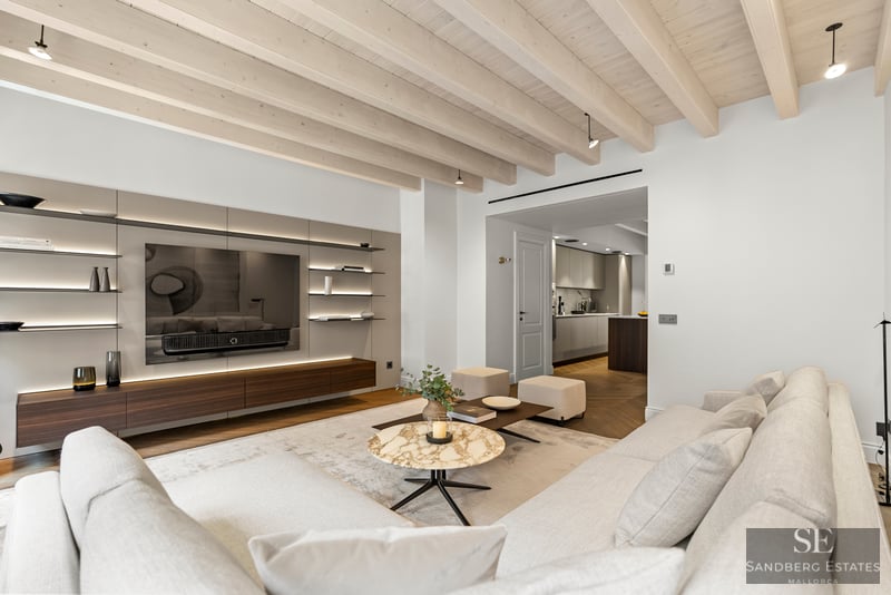 Salón moderno con sofás blancos, mesa de mármol, techo de vigas de madera y mueble de TV integrado.