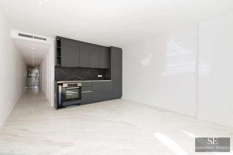 Modern kitchen area with dark gray cabinets, black marble backsplash, and white marble floors in a bright open room.