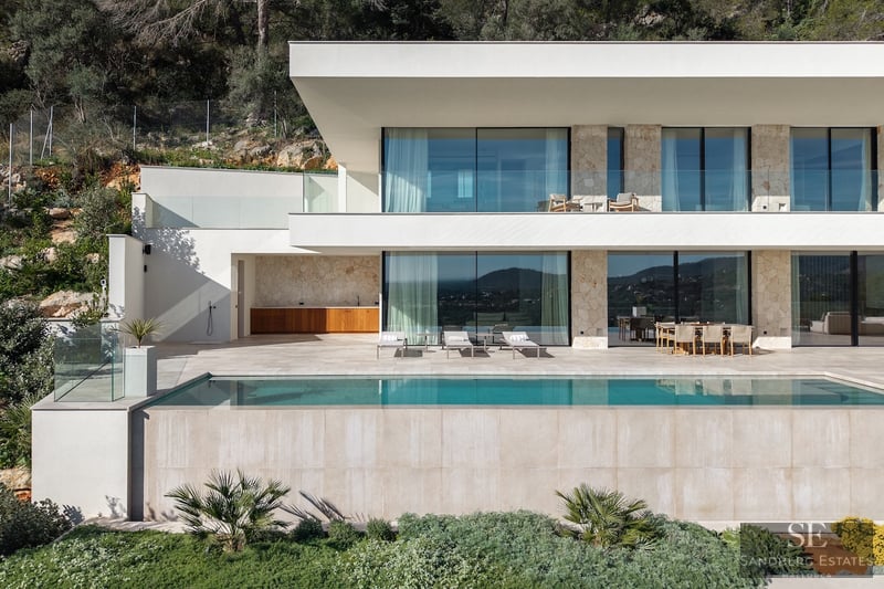 Modern two-story villa with a turquoise infinity pool, stone walls, large glass windows, and a sunny terrace.
