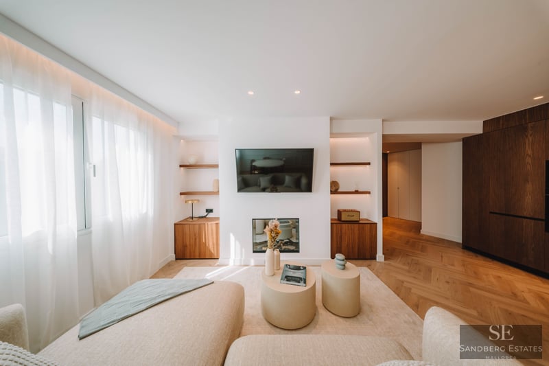 Bright living room featuring a wall-mounted TV, electric fireplace, herringbone wood floors, and cream sofas.