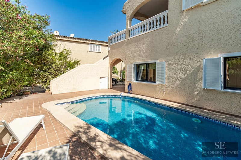 View of a pool surrounded by lawn and a modern two-story house with large windows. Natural lighting and minimalist design.
