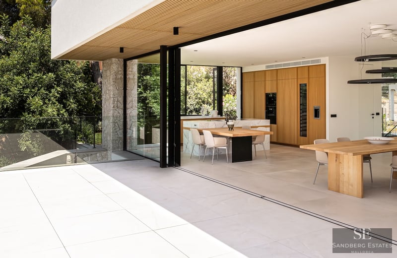 Modern kitchen with wood cabinets and marble island opening to a sunny stone terrace via large sliding glass doors.