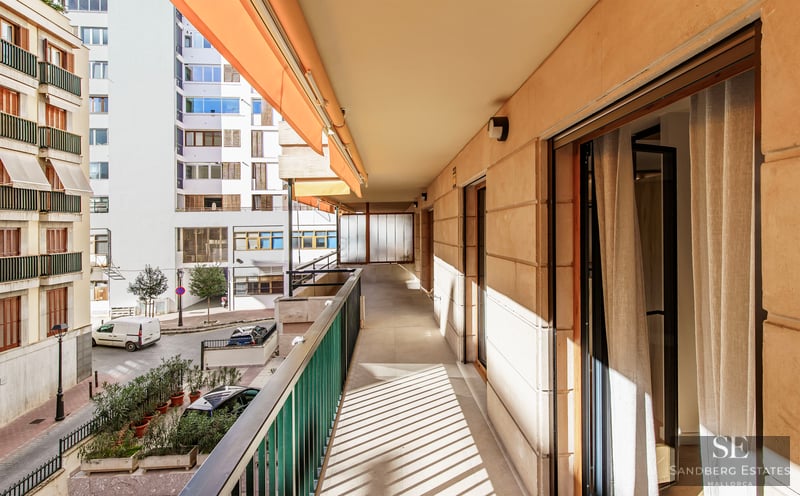 Lång solig balkong med orange markis och metallräcke med utsikt över en stadsgata.