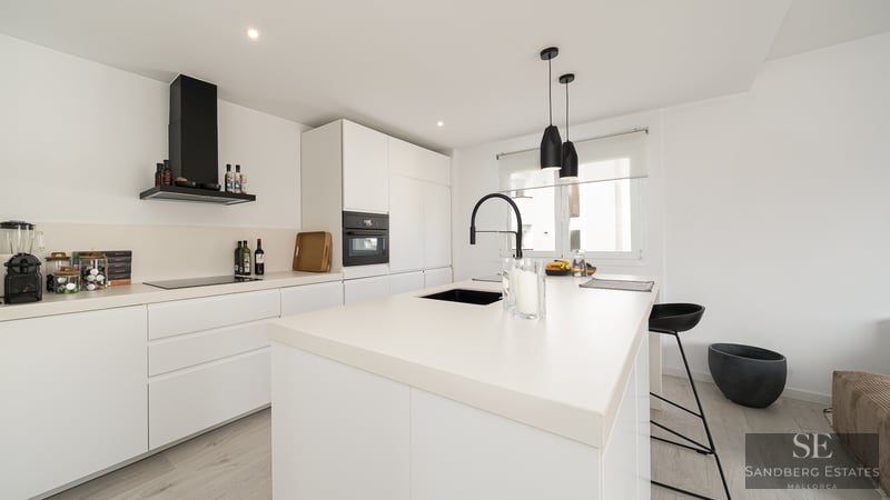 Modern white kitchen with a large island, black faucet, and sleek integrated appliances.