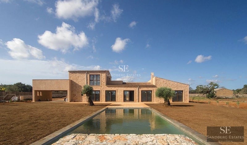 Spacious living room with large windows, modern fireplace, light wood floors, and designer furniture. Abundant natural light.