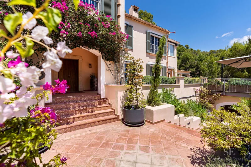 Terracotta steps leading to a wood door of a Mediterranean villa framed by pink bougainvillea.