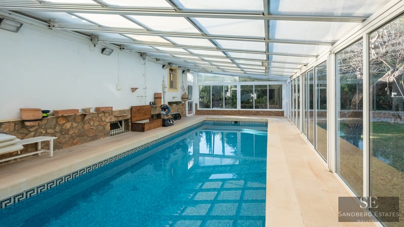 Indoor pool with blue mosaic tiles, stone accent wall, and translucent roof next to sliding glass doors.