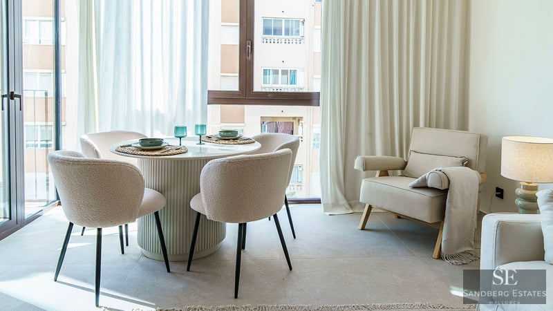 Heller Essbereich mit rundem weißem Tisch, vier Bouclé-Stühlen und großen Fenstern mit weißen Vorhängen.