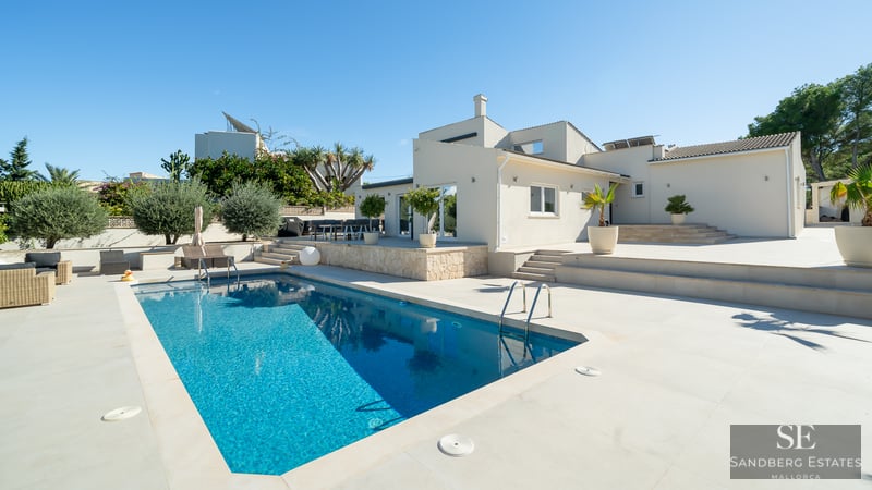 Piscine bleu éclatant à côté d'une villa blanche moderne avec une vaste terrasse en pierre sous un ciel dégagé.