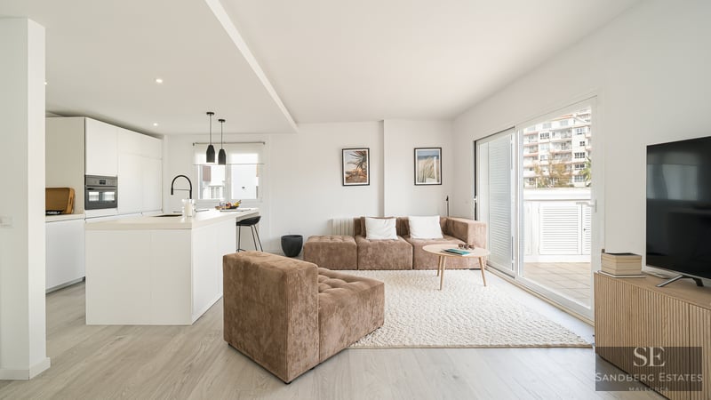 Bright modern living room with a brown corduroy modular sofa, textured rug, and a minimalist white kitchen.