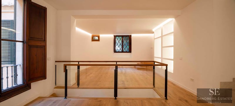A modern indoor landing with light oak flooring, glass railings, and warm cove lighting against white walls.