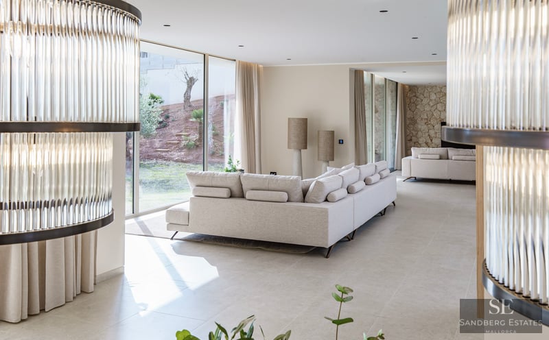 Spacious modern living room with cream sectional sofa, large glass walls viewing a garden, and stone accent wall.