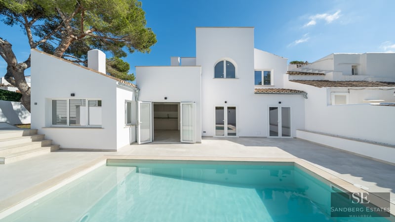 Turquoise swimming pool in front of a clean white modern Mediterranean villa under a clear blue sky.