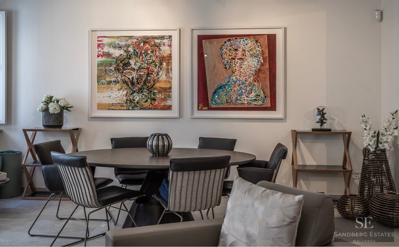 Modern dining room featuring a dark round table, designer chairs, and two large abstract paintings on a white wall.