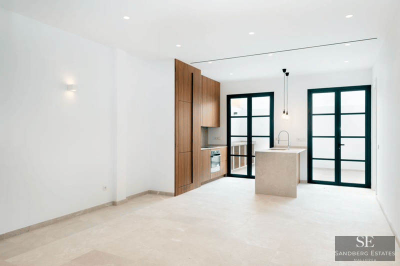 Moderne Küche mit Holzschränken, Steininsel und großen schwarz gerahmten Glastüren, die zur Terrasse führen.