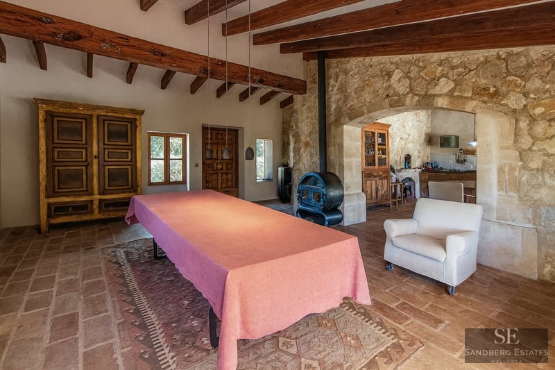 Large table with a pink cloth in a rustic room featuring wooden beams, stone walls, and a wood-burning stove.