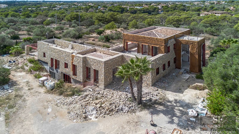 Vista elevada de una gran villa de lujo con paredes de piedra en construcción rodeada de vegetación mediterránea.