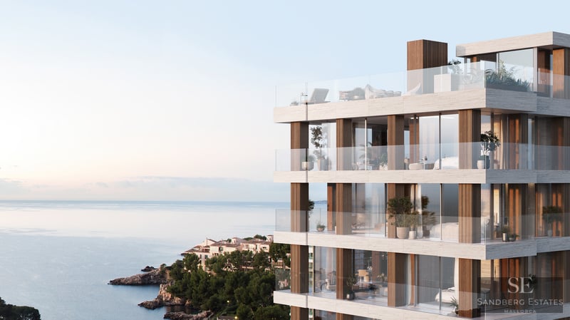 Modern multi-story building with stone facade, glass balconies, and panoramic sea views at sunset.