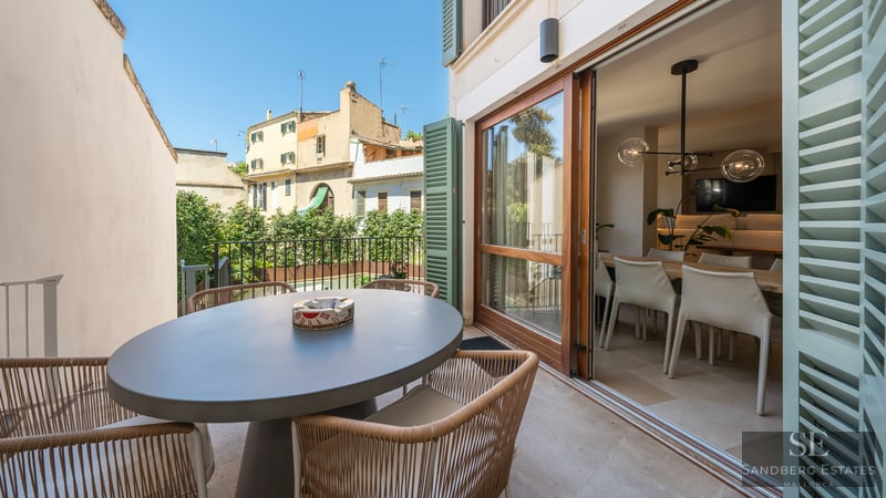Sunny terrace with a gray oval dining table and wicker chairs next to large sliding glass doors.