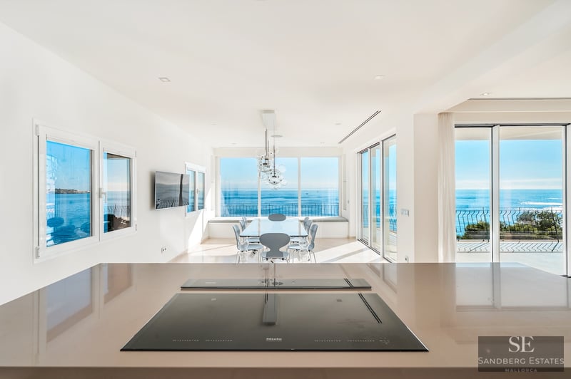 Närbild på köksö med induktionshäll med utsikt över matplats och stora fönster mot det blå havet.