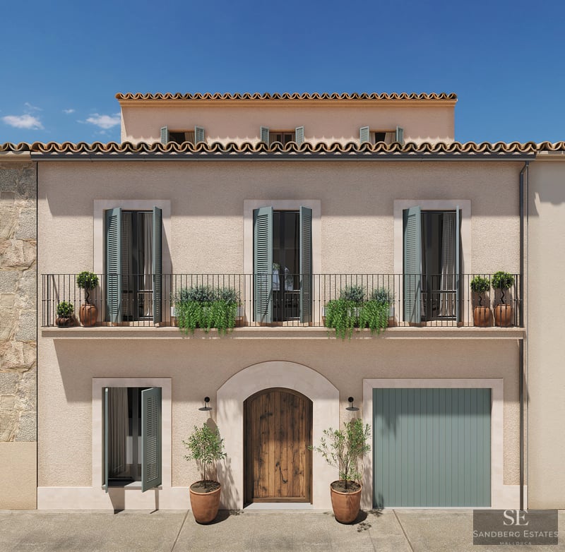 Fachada de tres niveles con paredes de estuco beige, contraventanas verde salvia, balcón de hierro y puerta de madera.