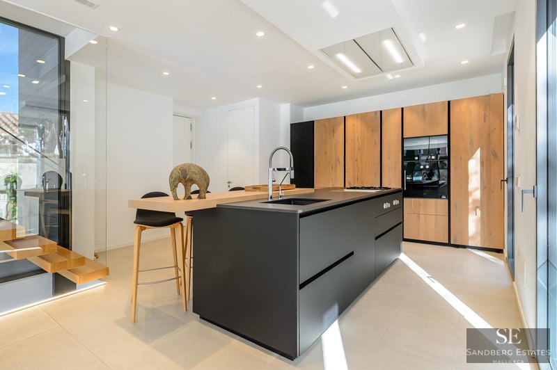 Modern kitchen with a large black island, wood cabinets, and integrated appliances under bright lighting.